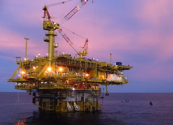 Offshore oil and gas production platform lit up at dusk with a support vessel alongside